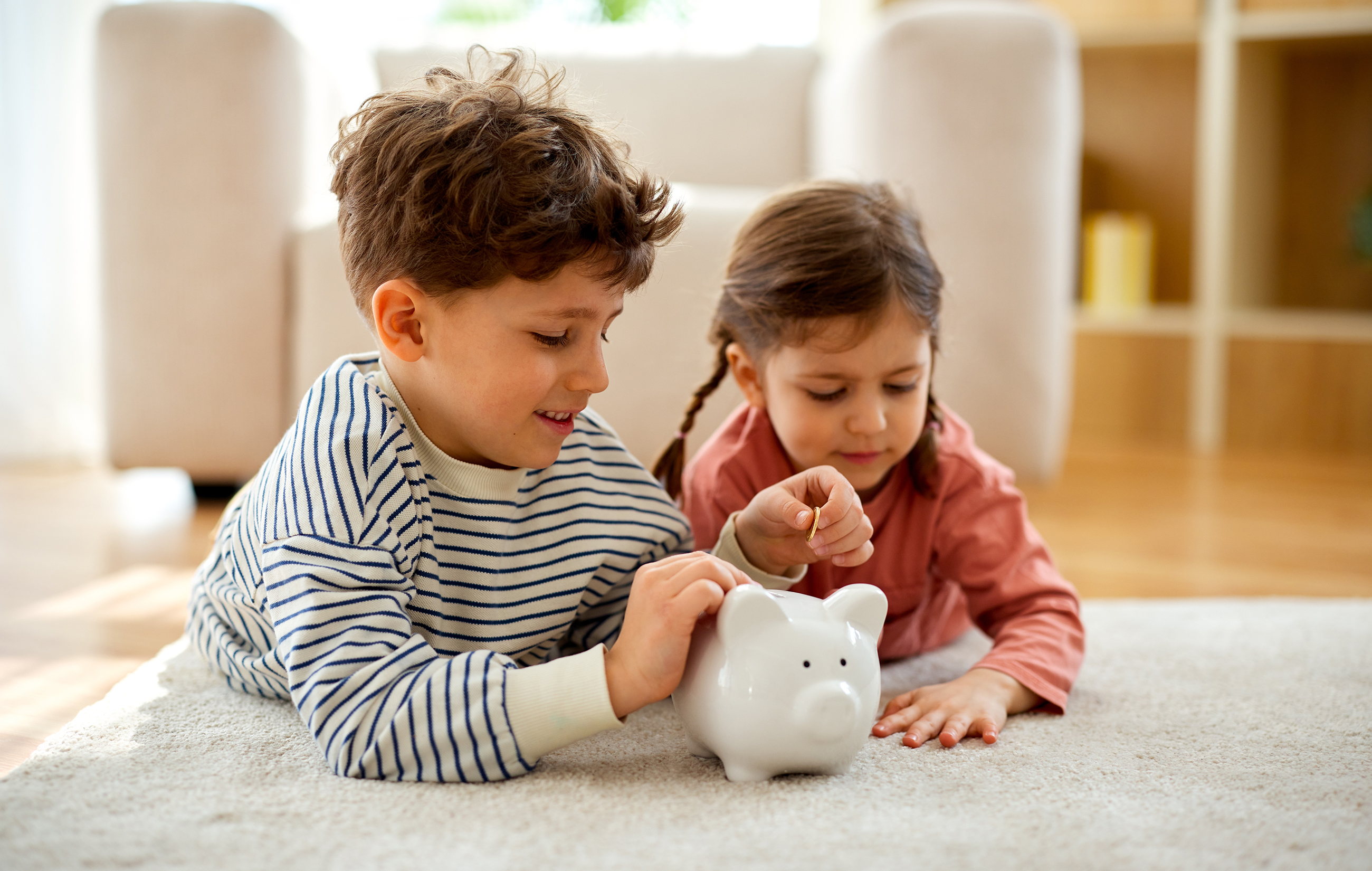 Children,Putting,Coins,Into,Piggy,Bank,At,Home